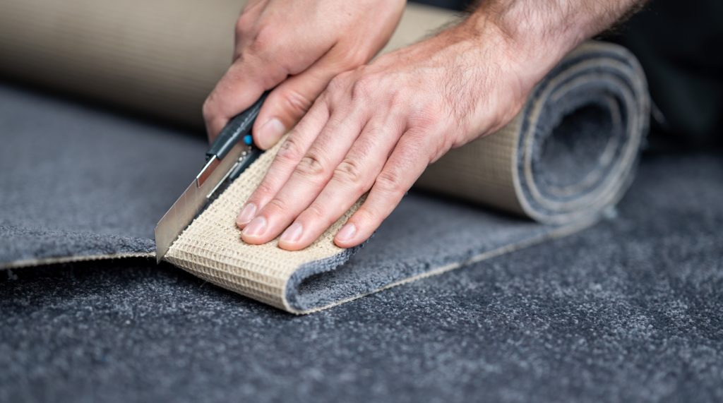Handyman cutting a new carpet with a carpet cutter..