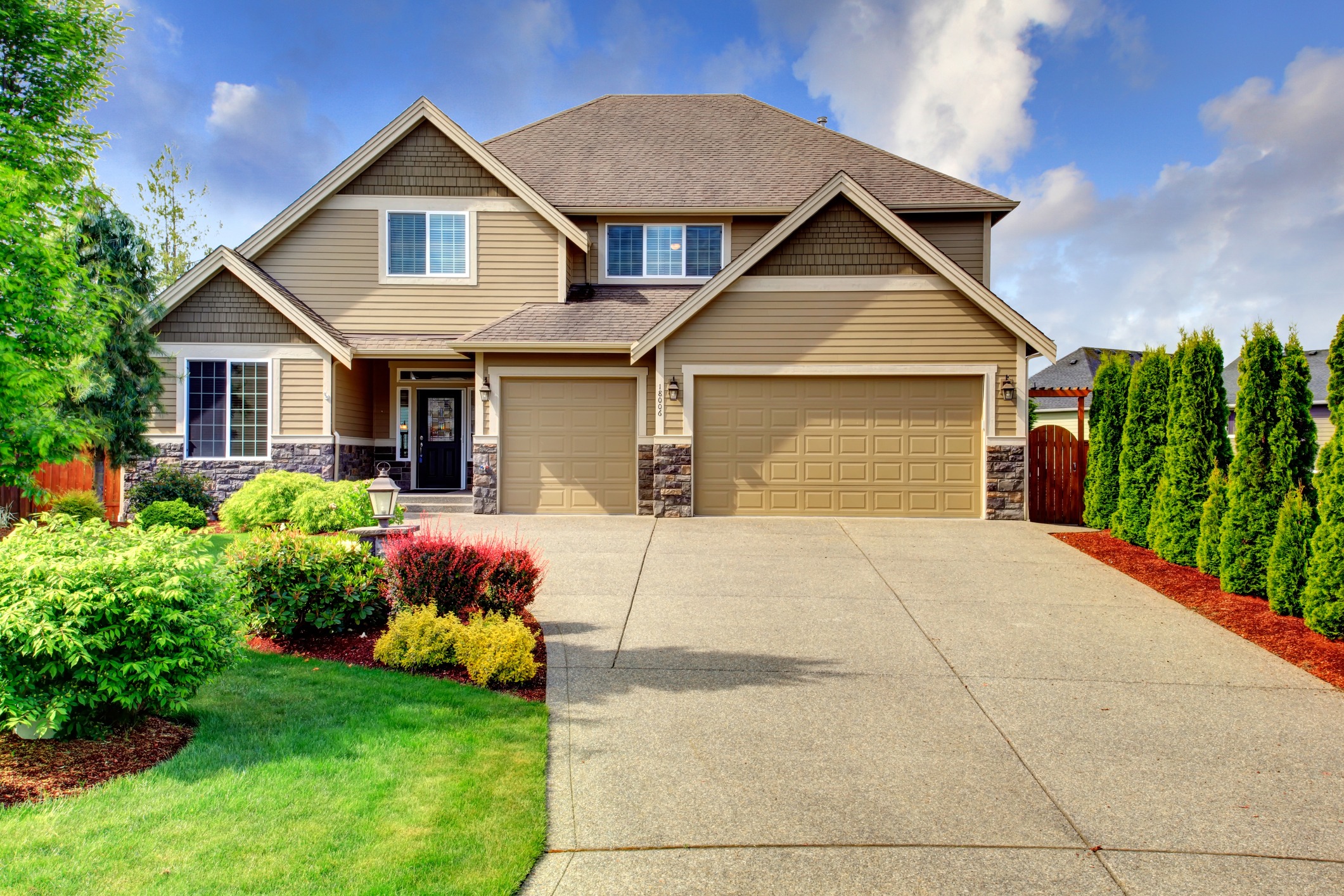 Beige luxury house tih stone trim base. View of porch, garage and driveway